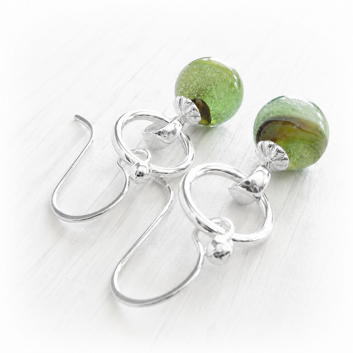 Sterling silver earrings with small green and brown glass marbles containing cremation ashes of a loved one