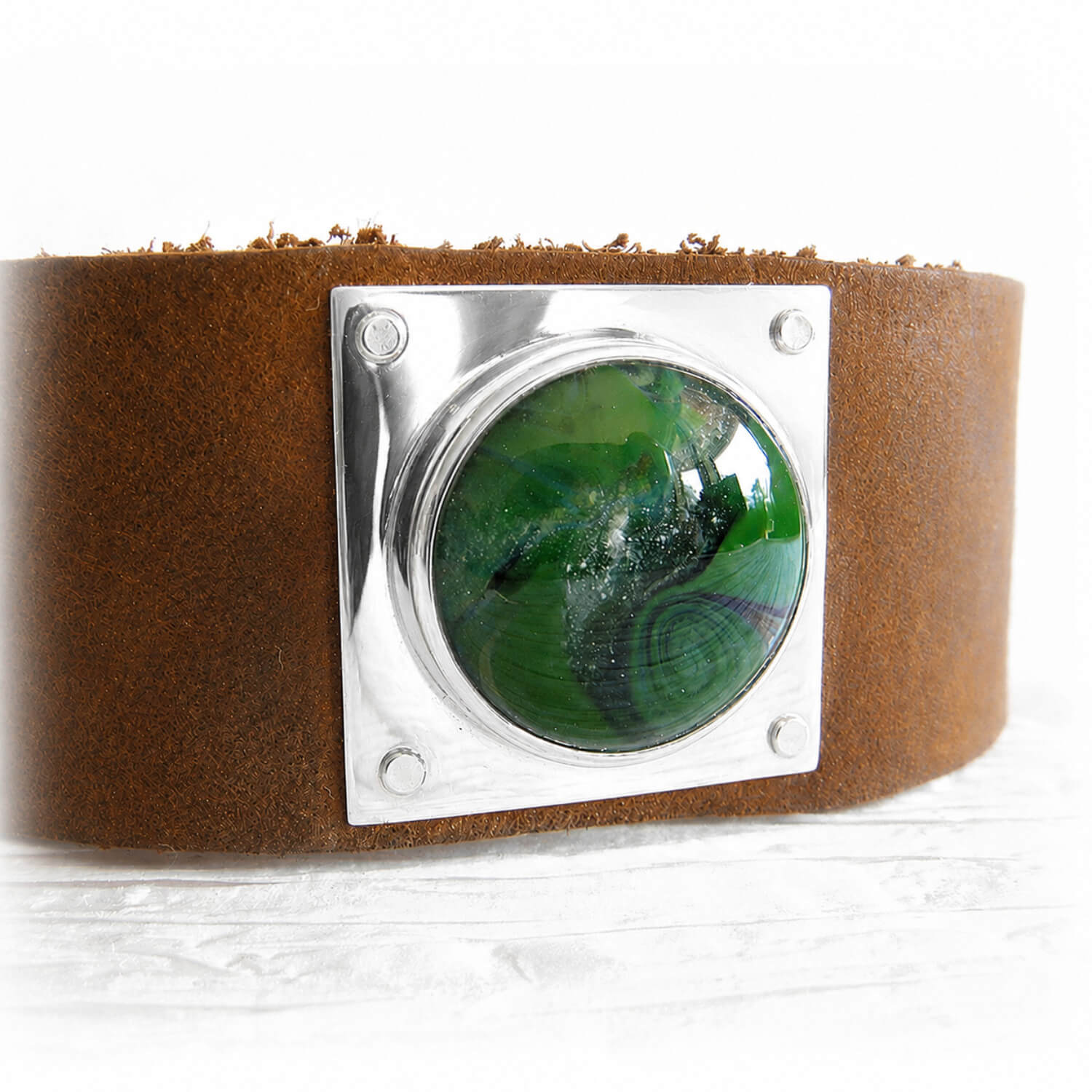 White pet ashes encased in swirls of hand blown green glass on a sterling silver and brown leather cuff bracelet