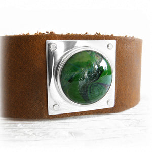 White pet ashes encased in swirls of hand blown green glass on a sterling silver and brown leather cuff bracelet