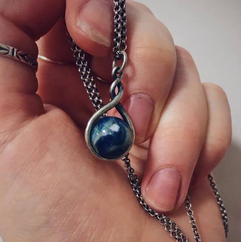 Hand holding a necklace with a blue pendant