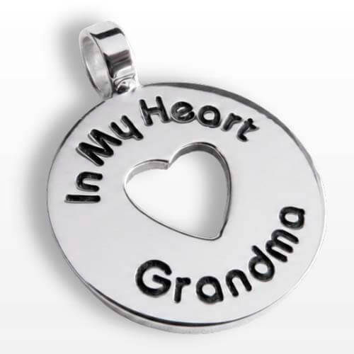 A silver round pendant charm with a cutout heart in the center and the words 'In My Heart Grandma' engraved around the edge, shown on a light gray background.