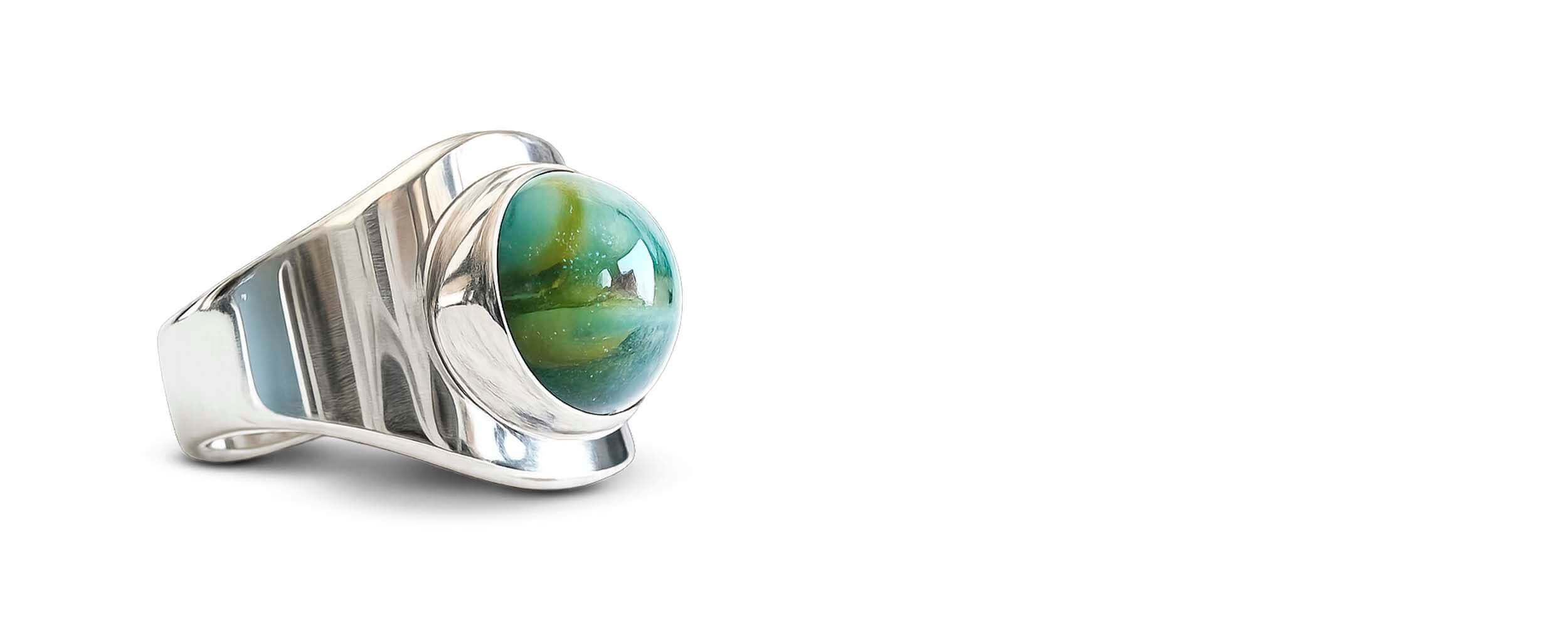 Silver ring with a round, glass cremation ash cabochon on a white background