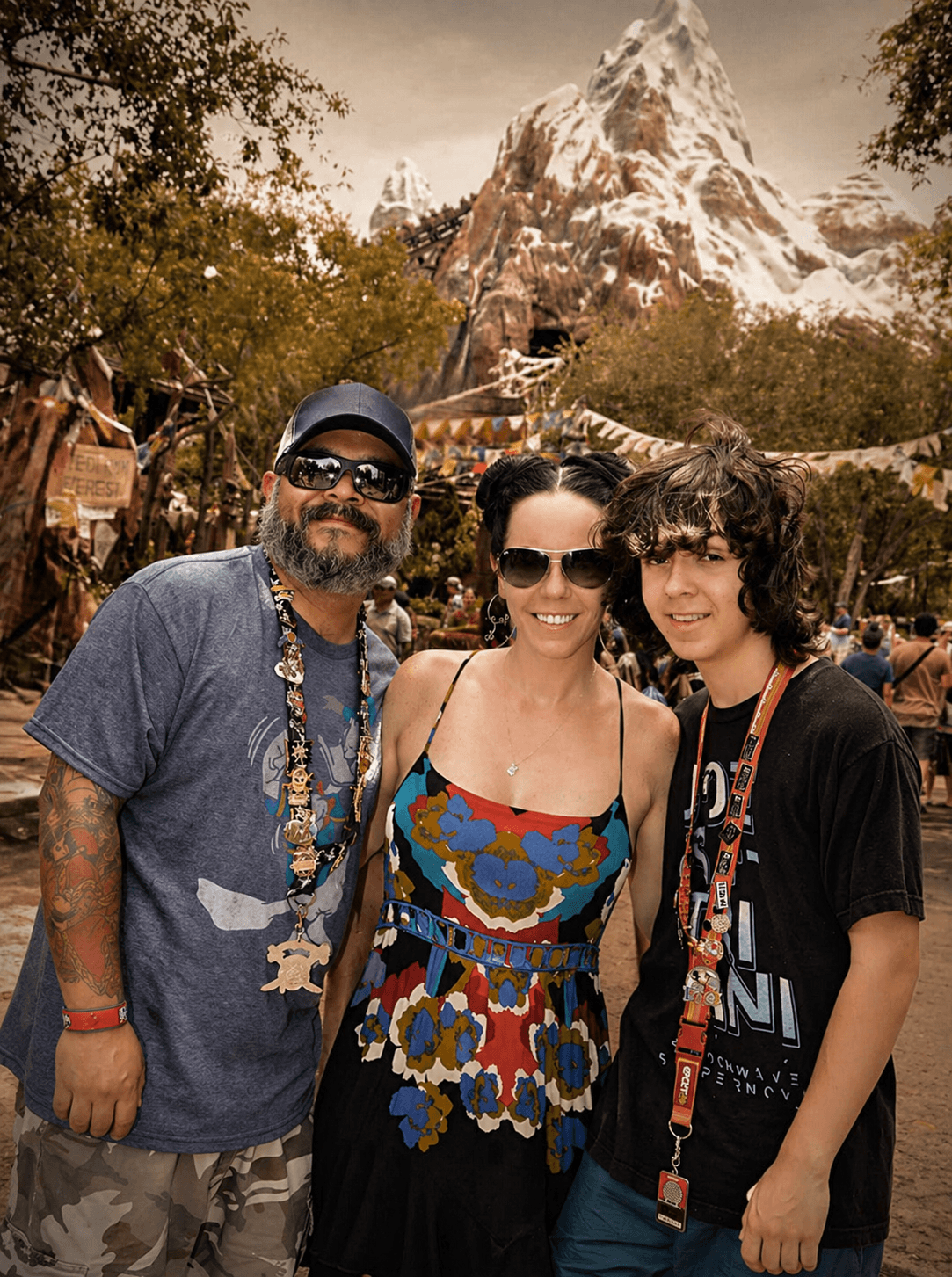 Three people posing in front of a mountainous landscape with trees.