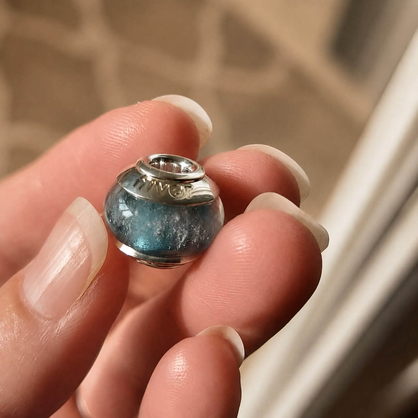Close-up of a hand holding a blue glass memorial bead with sterling silver bead caps 