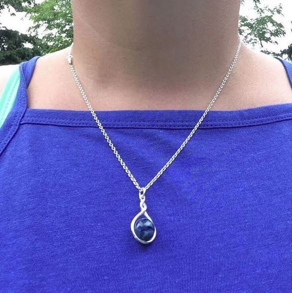 Necklace with a blue pendant worn by a person in a blue top outdoors.