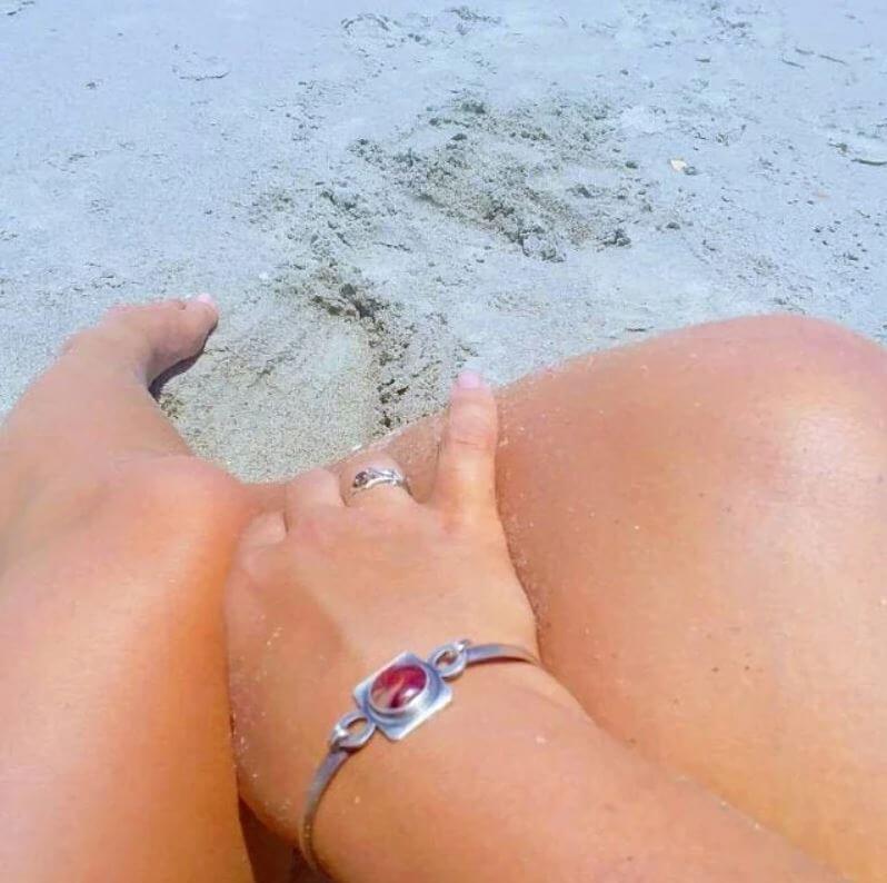 Close-up of a person's legs with silver bracelets on a sandy surface