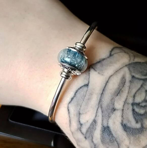 Silver bracelet with a blue bead on a wrist with tattoos