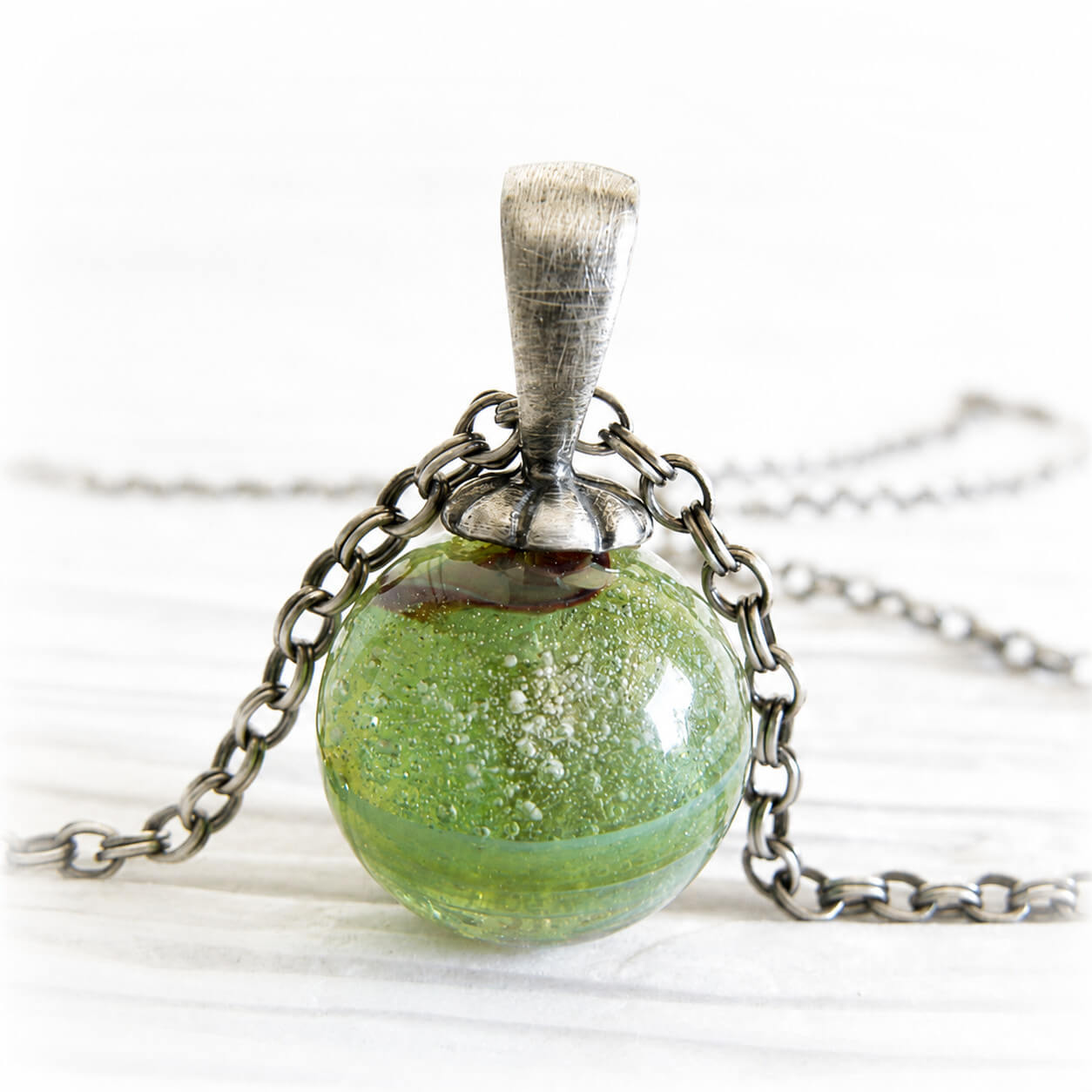 Green memorial marble with floating ashes visible within the glass set on a sterling silver necklace with an antique finish