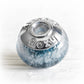 Blue glass cremation bead with custom engraved sterling silver bead caps on a white background 