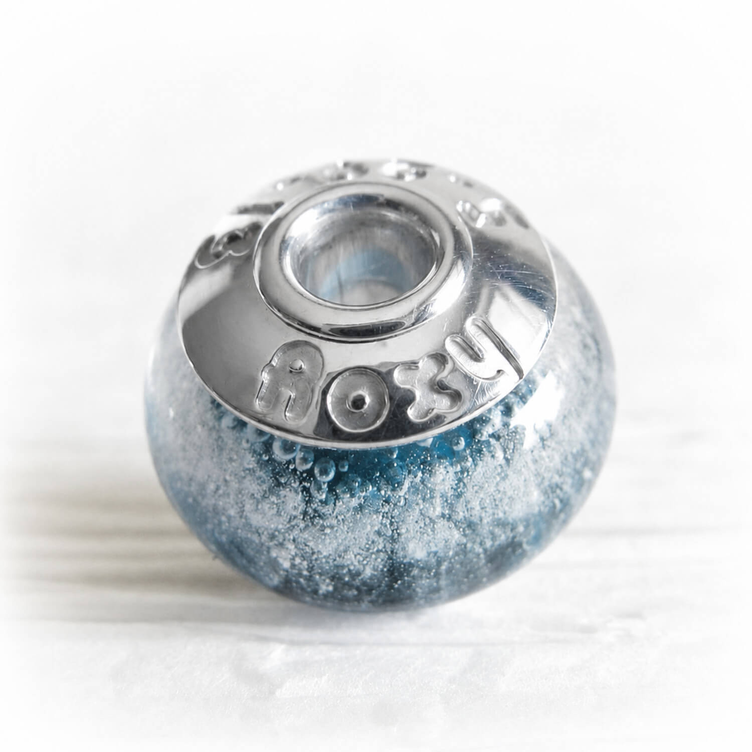 Blue glass cremation bead with custom engraved sterling silver bead caps on a white background 