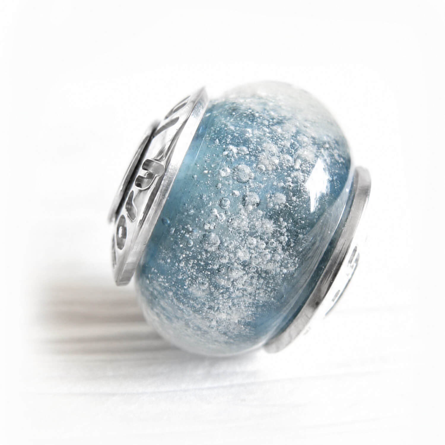Hand blown glass cremation bead with personalized sterling silver bead caps on a white background 