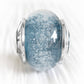 Cremation ashes encased in a blue hand crafted glass bead on white background 