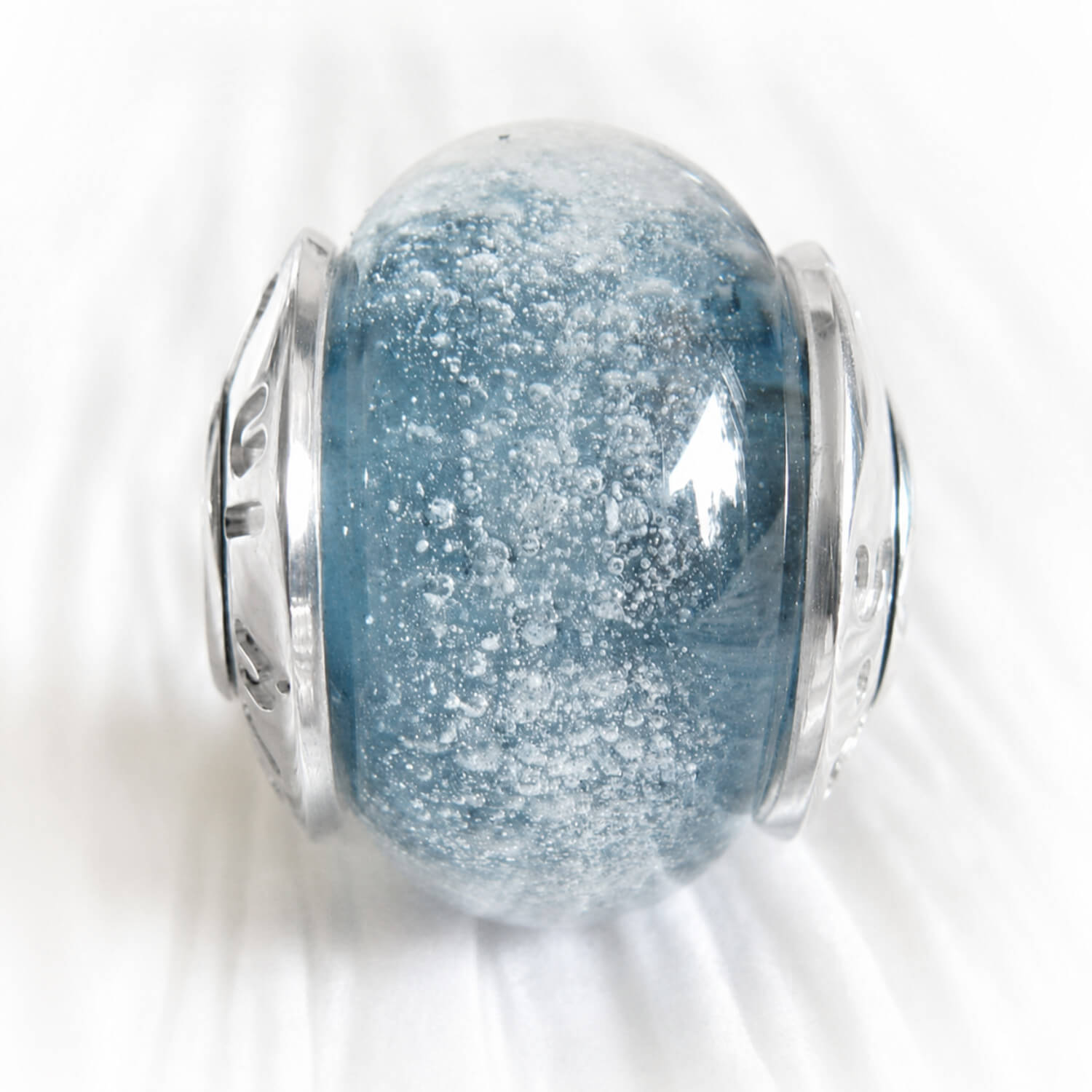 Cremation ashes encased in a blue hand crafted glass bead on white background 