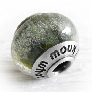 Green and blue glass bead encased  with floating cremation ashes 