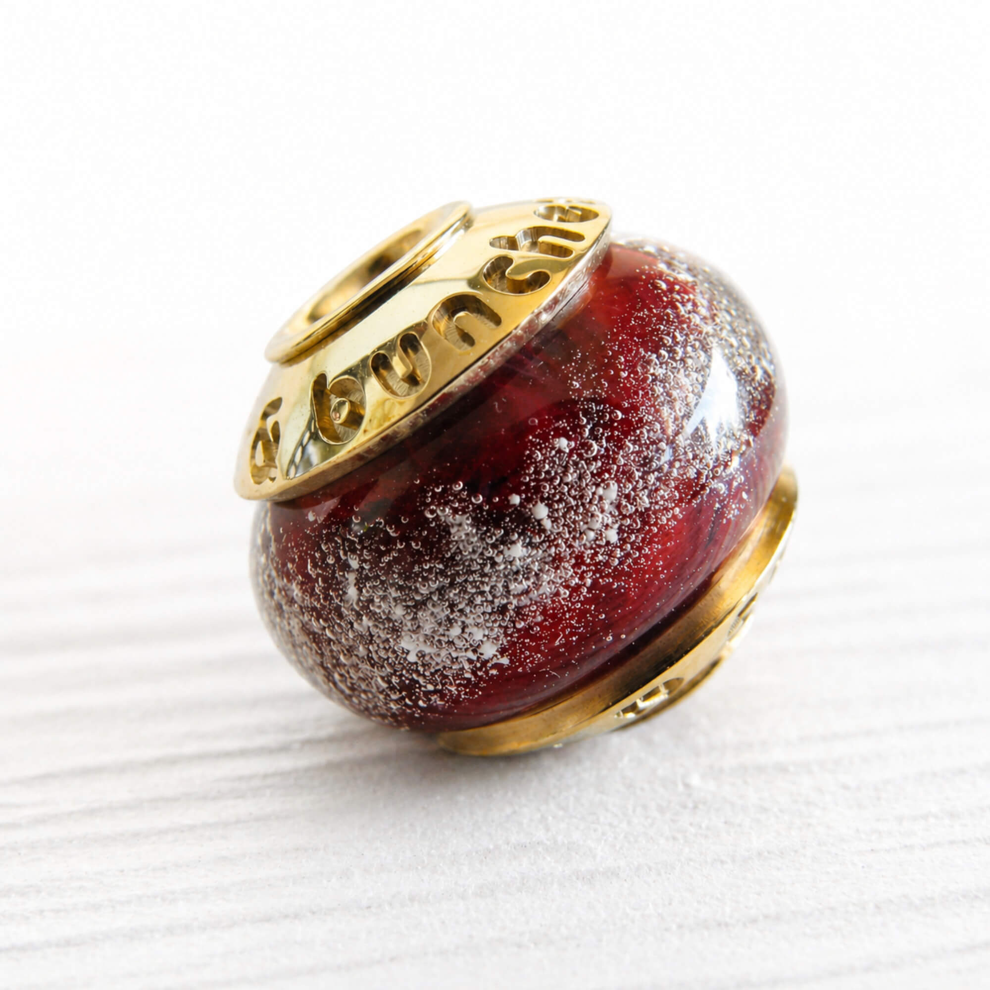 Red glass cremation ash memorial bead with gold cap on a white background