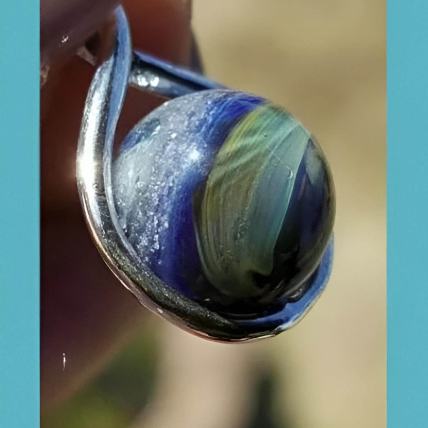 Close-up of a marbled blue and green bead with a silver ring.
