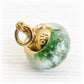 Gold charm bead with a green glass and white ashes suspended within the glass