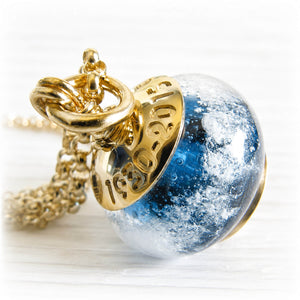 Gold necklace engraved with custom text and a blue hand blown glass bead with cremation ashes sealed within the glass