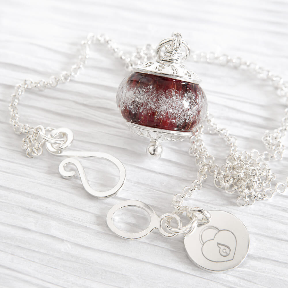 Deep red hand-crafted memorial bead with encased ashes set in sterling silver on a white background