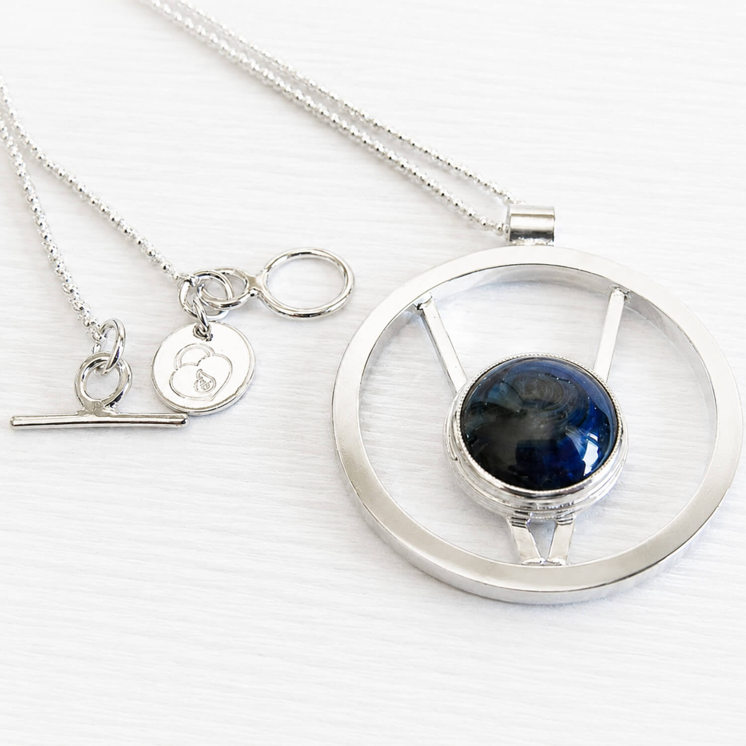 Hand forged sterling silver memorial necklace with a Locked In Art logo tag featuring an ash infused blue glass centerpiece 