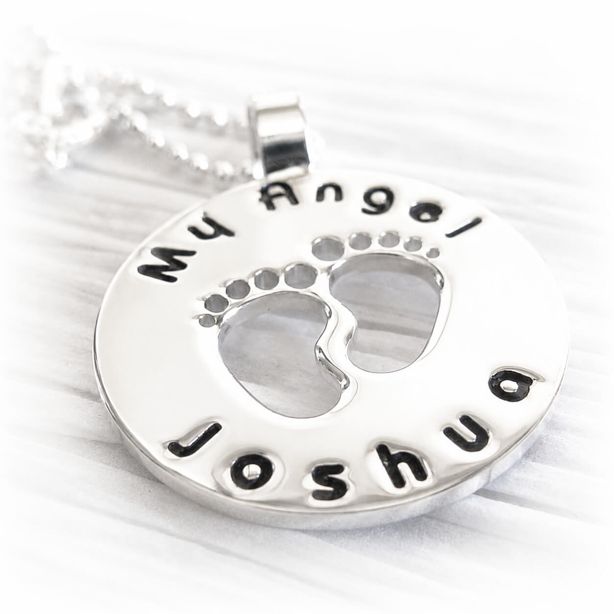Silver pendant with footprints and engraved personalized text on a white background