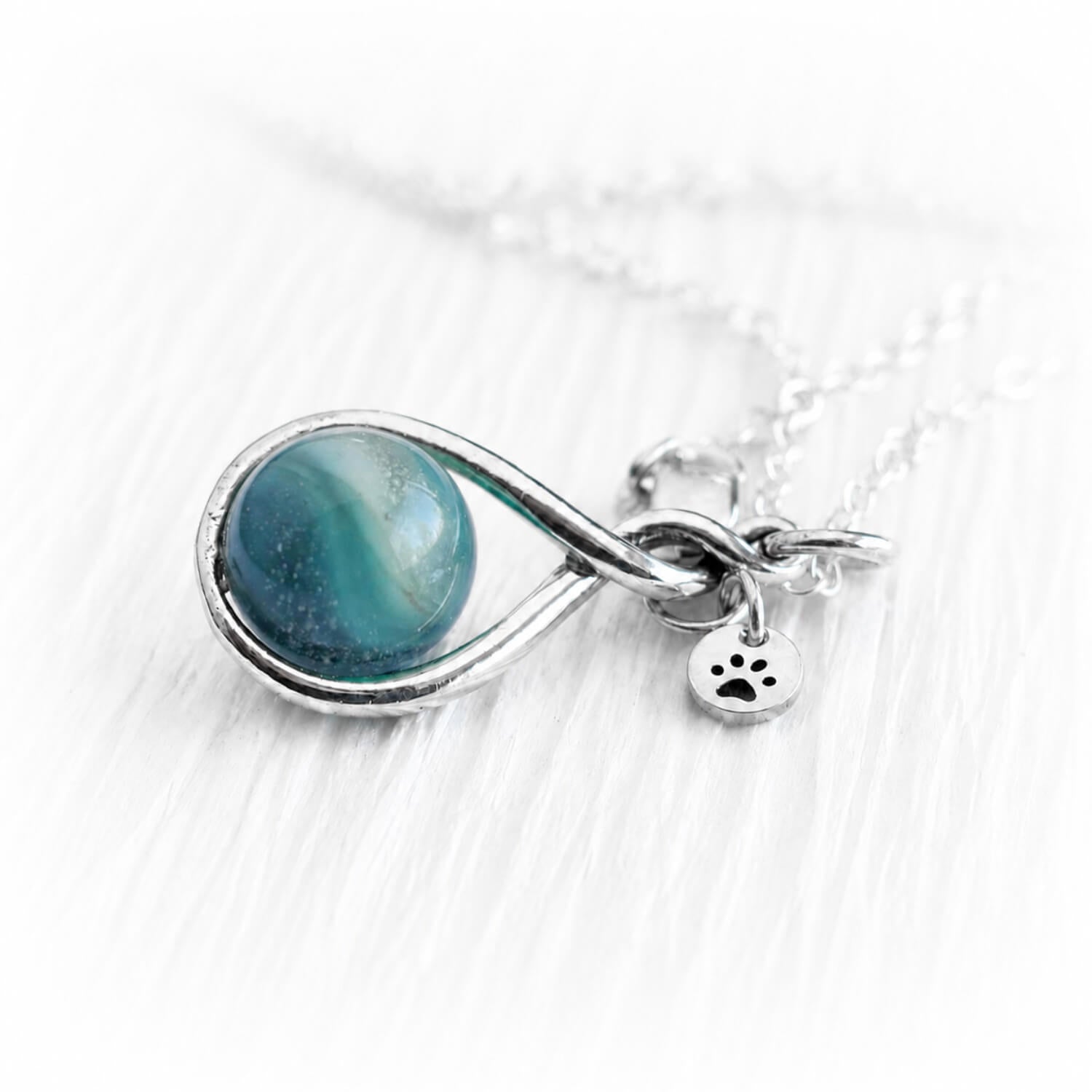 Necklace teardrop pendant featuring a hand blown glass memorial marble and a tiny paw charm on a white 