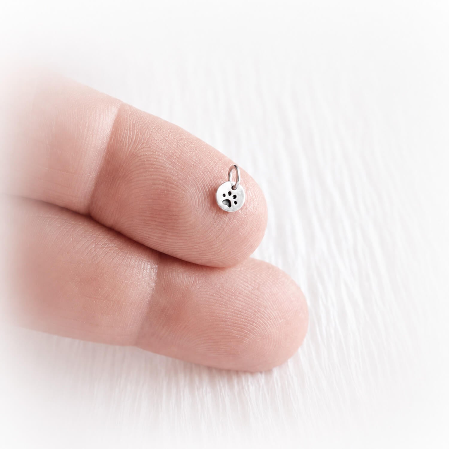 Small silver paw print charm on a finger against a white background