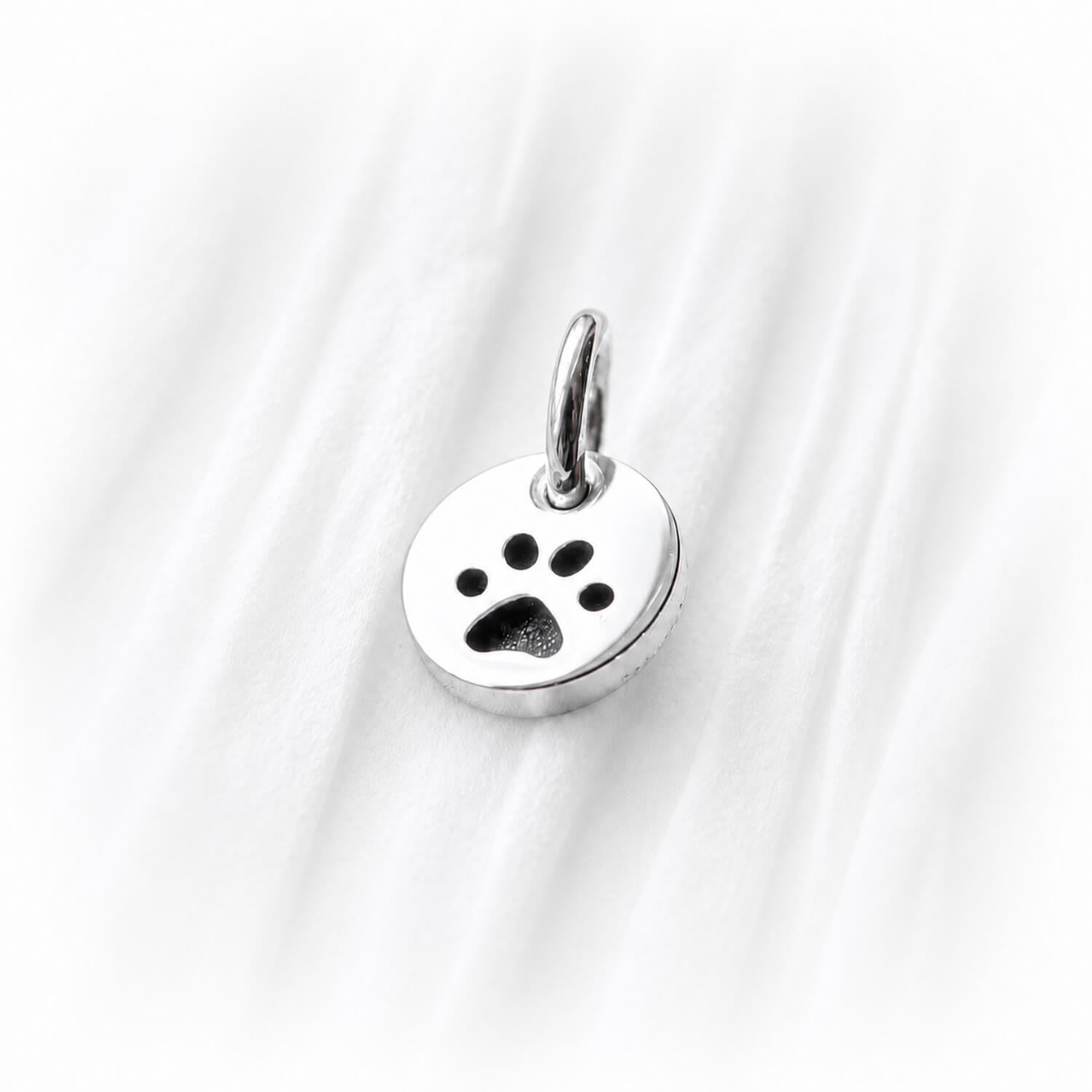 Silver paw print charm on a white fabric background
