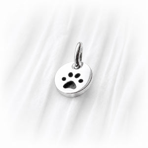 Silver paw print charm on a white fabric background