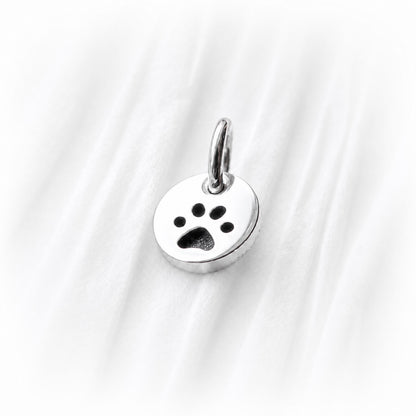 Silver paw print charm on a white fabric background