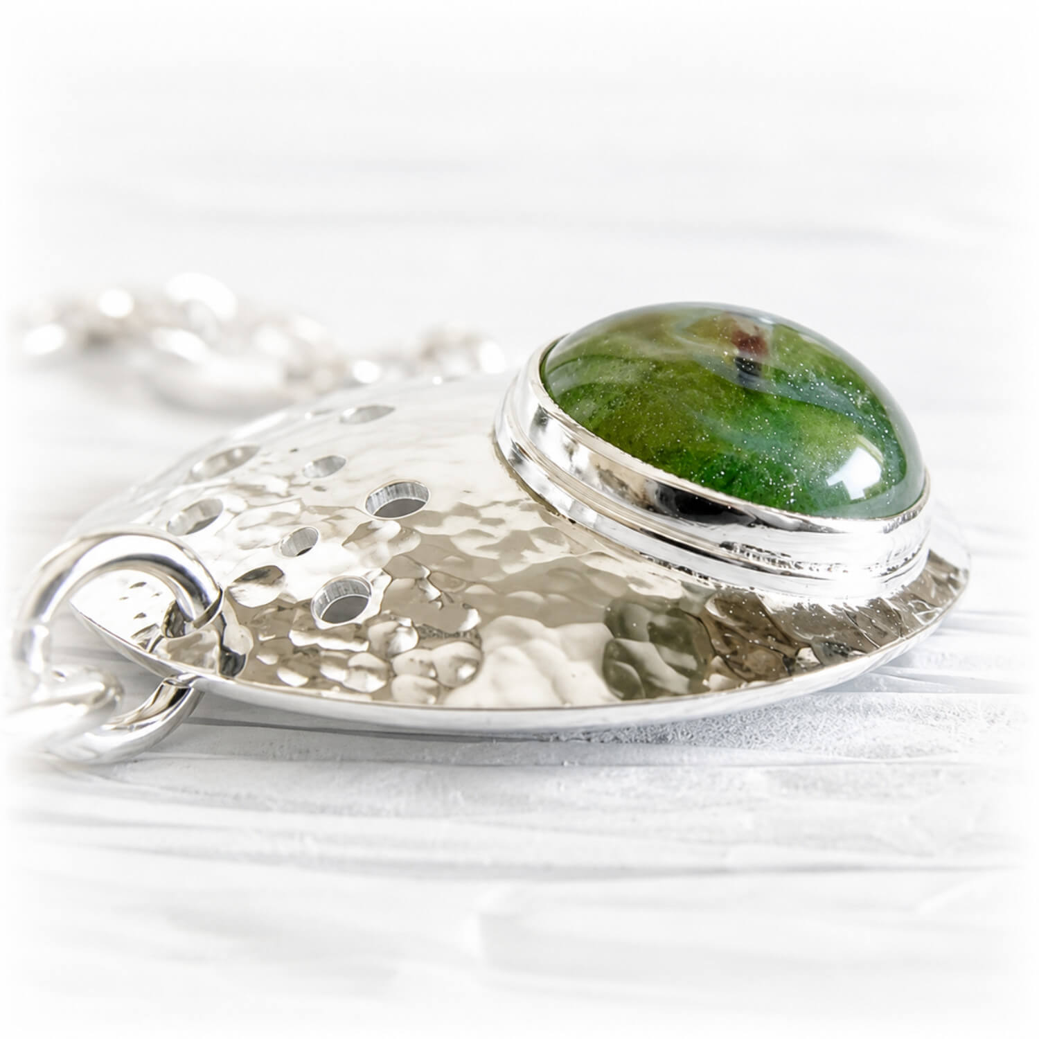 A hand forged sterling silver bracelet focal piece featuring a green hand blown glass cremation gem