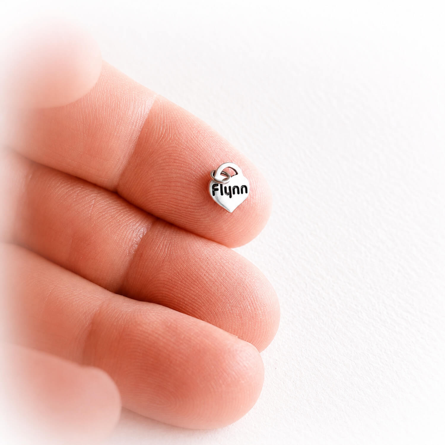 Silver heart-shaped sterling silver charm with your choice of engraving resting on a finger against a white background