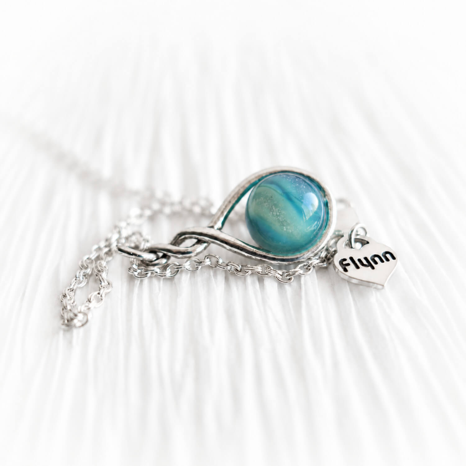 Memorial necklace with an aqua colored cremation glass marble and a tiny personalized heart charm