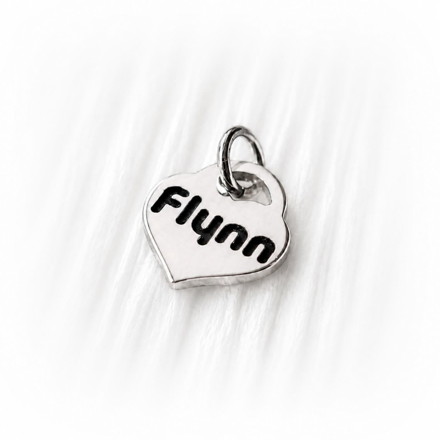 Silver heart-shaped charm with 'Flynn' engraved on a white fabric background