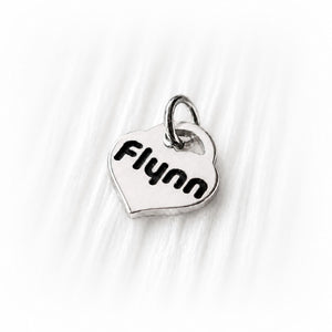 Silver heart-shaped charm with 'Flynn' engraved on a white fabric background