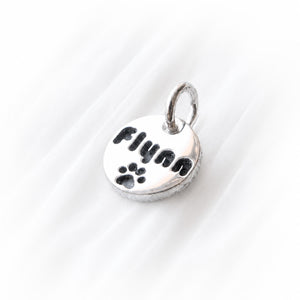 Silver charm engraved with 'Flynn' and a tiny paw print on a white background